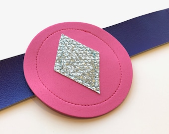 May include: A pink circle with a silver diamond shape in the center. The circle is attached to a purple strap.
