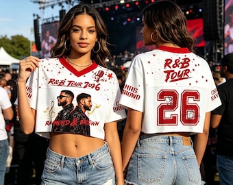 May include: White cropped jersey with red trim and the text "R&B TOUR 2026". The jersey features a graphic of two men and musical notes. The number "26" is on the back. The models are wearing denim shorts.