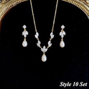 May include: A gold-toned jewelry set consisting of a necklace and two drop earrings. The necklace features marquise-cut clear stones arranged in a leaf pattern with a central teardrop pearl. Each earring mirrors this design with a pearl drop.