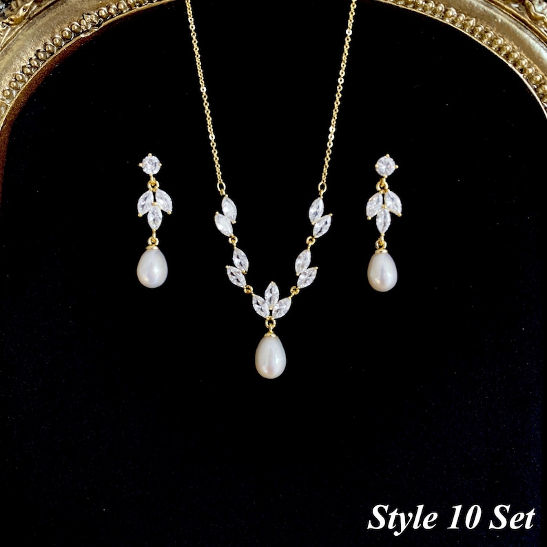 May include: A gold-toned jewelry set consisting of a necklace and two drop earrings. The necklace features marquise-cut clear stones arranged in a leaf pattern with a central teardrop pearl. Each earring mirrors this design with a pearl drop.