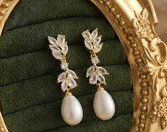 May include: A pair of gold-toned drop earrings featuring a vertical arrangement of marquise-cut clear crystals in a leaf-like pattern, terminating in a single, smooth, teardrop-shaped white pearl suspended from the base of the crystal setting.