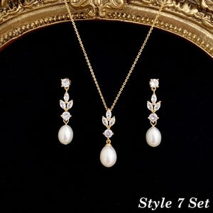 May include: A gold-tone jewelry set consisting of a necklace and two drop earrings. Each piece features a white teardrop pearl suspended from a cluster of clear marquise and round-cut stones. The necklace includes a delicate gold chain. Style 7 Set.
