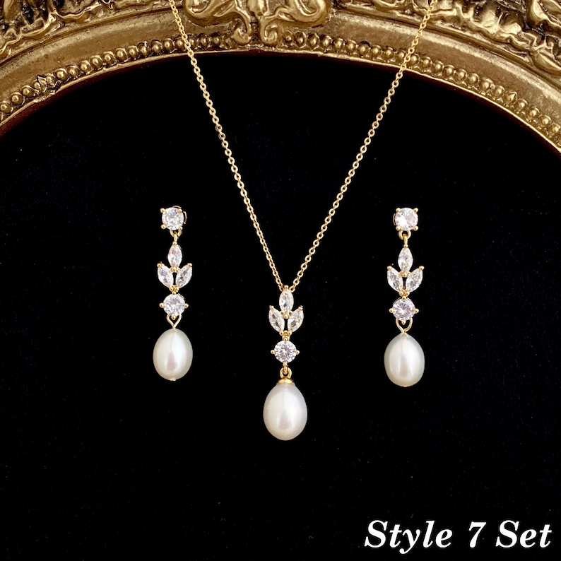 May include: A gold-tone jewelry set consisting of a necklace and two drop earrings. Each piece features a white teardrop pearl suspended from a cluster of clear marquise and round-cut stones. The necklace includes a delicate gold chain. Style 7 Set.