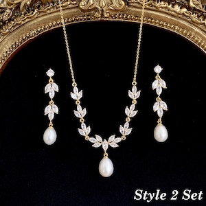 May include: A gold-toned jewelry set consisting of a necklace and two drop earrings. Each piece features marquise-cut clear stones arranged in a leaf-like pattern, accented with a single white teardrop pearl. The text Style 2 Set is visible.