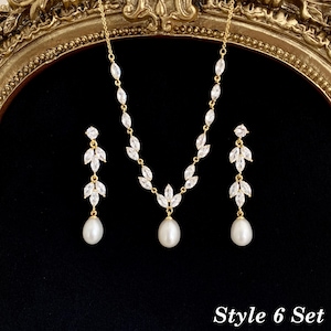 May include: A gold-toned jewelry set consisting of a necklace and two drop earrings. The necklace features marquise-cut clear stones arranged in a leaf pattern with a central white pearl drop. Each earring mirrors this leaf design with a pearl.