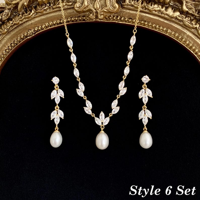 May include: A gold-toned jewelry set consisting of a necklace and two drop earrings. The necklace features marquise-cut clear stones arranged in a leaf pattern with a central white pearl drop. Each earring mirrors this leaf design with a pearl.