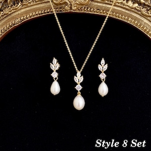 May include: A gold-toned jewelry set consisting of a necklace and two matching earrings. Each piece features a teardrop-shaped white pearl suspended below a round clear stone and a leaf-shaped cluster of clear stones. Text reads Style 8 Set.