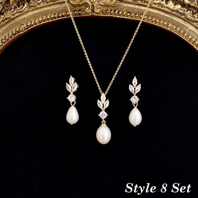 May include: A gold-toned jewelry set consisting of a necklace and two matching earrings. Each piece features a teardrop-shaped white pearl suspended below a round clear stone and a leaf-shaped cluster of clear stones. Text reads Style 8 Set.