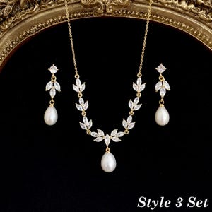 May include: A gold-toned jewelry set consisting of a necklace and two matching earrings. The necklace features a chain with marquise-cut clear stones arranged in leaf-like patterns, ending in a single white teardrop pearl pendant. The earrings mirror this design with a small stud, leaf-shaped stones, and a dangling white pearl. The text "Style 3 Set" is visible in the bottom right corner.