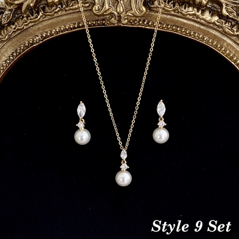 May include: A gold-toned jewelry set consisting of a necklace and two matching drop earrings. Each piece features a white pearl suspended below a small clear marquise-cut stone. The necklace has a delicate chain. The text Style 9 Set is visible.
