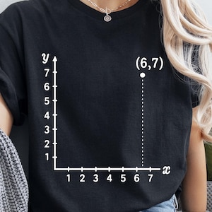 May include: Black t-shirt with a white coordinate plane graphic. The graphic includes the point (6,7) plotted on the graph. The x-axis is labeled from 1 to 7, and the y-axis is labeled from 1 to 7.
