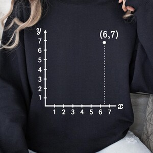 May include: Black sweatshirt featuring a white graph with the coordinates (6,7). The graph has x and y axes with numbered increments. The sweatshirt is a solid black color.