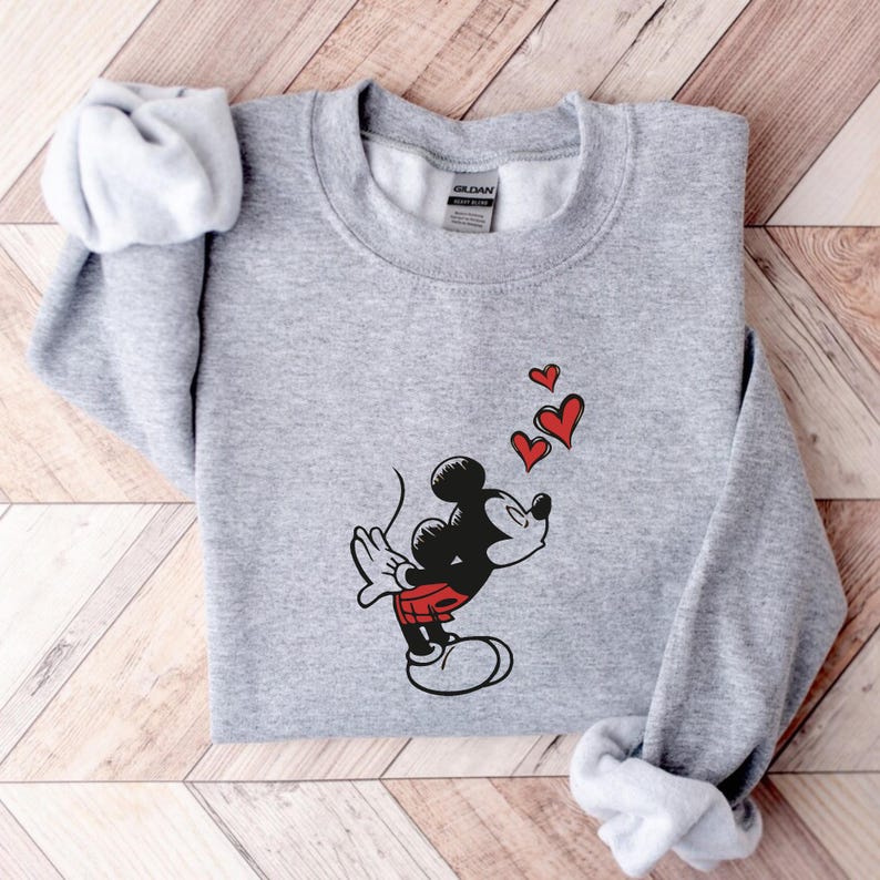 K&ouml;nnte beinhalten: Hellgraues Sweatshirt mit einer Grafik von Mickey Mouse, die drei rote Herzen pustet. Mickey ist in Schwarz, Rot und Wei&szlig; dargestellt. Das Sweatshirt hat einen Rundhalsausschnitt und lange &Auml;rmel.