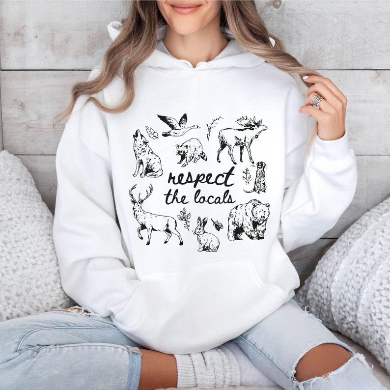 Puede incluir: Sudadera blanca con un gr&aacute;fico en blanco y negro de varios animales norteamericanos, incluyendo un lobo, un oso y un ciervo. La frase "respect the locals" est&aacute; impresa en un estilo manuscrito. La sudadera tiene un bolsillo delantero y una capucha con cord&oacute;n.