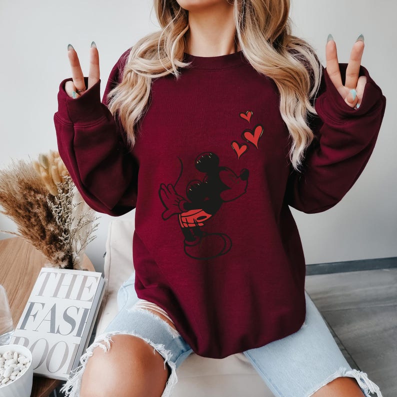 K&ouml;nnte beinhalten: Ein weinrotes Sweatshirt mit einer schwarzen und roten Mickey Mouse Grafik und drei roten Herzen. Das Sweatshirt hat lange &Auml;rmel und einen Rundhalsausschnitt. Das Design ist auf der Vorderseite zentriert.