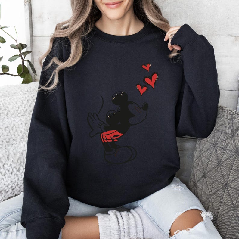 K&ouml;nnte beinhalten: Marineblaues Sweatshirt mit einer schwarzen Zeichentrickfigur mit roten Shorts und drei roten Herzen. Die Figur wirft K&uuml;sse. Ein l&auml;ssiges Oberteil.