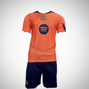 May include: Orange soccer jersey and navy blue shorts set. The jersey features a Spotify logo and a team crest. The shorts have a team logo on the leg. The jersey has navy blue trim.
