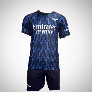 May include: A navy blue soccer uniform with a blue and white zigzag pattern. The shirt has the text "Emirates FLY BETTER" in white. The uniform includes a matching pair of navy blue shorts.
