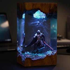 Può includere: Lampada rettangolare in legno con una figura di Darth Vader racchiusa in resina trasparente. La resina è illuminata da luci blu e viola, creando un effetto galattico. Design scuro e suggestivo.