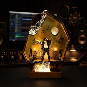May include: A decorative resin lamp featuring a miniature figure of a performer in a black suit and fedora, standing before a gate labeled Neverland. The scene includes musical notes, a disco ball, and silhouettes, all encased in a gold-toned frame.