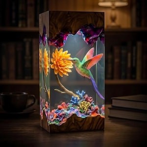 May include: A rectangular lamp featuring a clear resin block encased in wood at the top and bottom. Inside, a green and orange hummingbird hovers near a yellow flower, surrounded by colorful coral-like structures and purple accents.