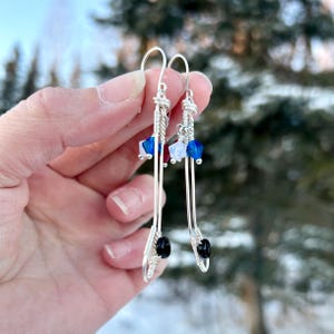 May include: A pair of silver earrings with black beads and blue, white, and red crystal accents. The earrings are dangle style and feature a wire design.