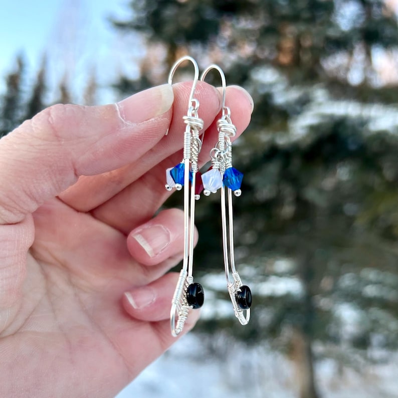 May include: A pair of silver earrings with black beads and blue, white, and red crystal accents. The earrings are dangle style and feature a wire design.