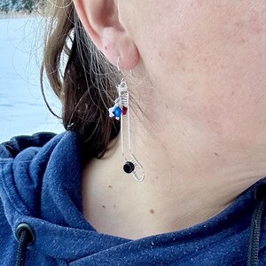 May include: Silver wire earrings shaped like a sock with red, blue, and white beads.