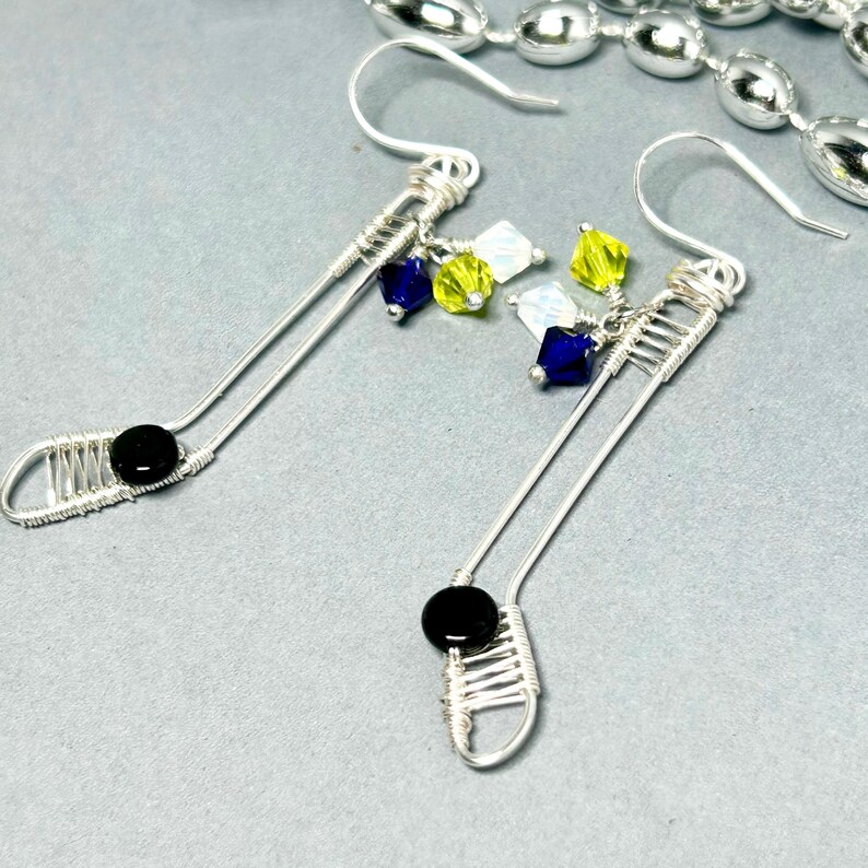 May include: A pair of silver wire earrings with black, blue, white, and yellow crystal beads. The earrings are long and dangle.
