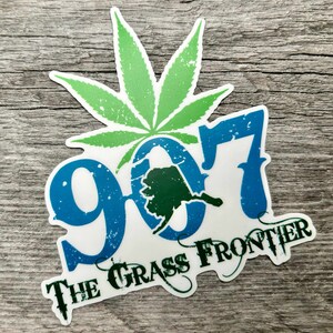 May include: A sticker with a green cannabis leaf above the blue and white text "907" with a green outline of Alaska. The words "THE GRASS FRONTIER" are below the numbers.