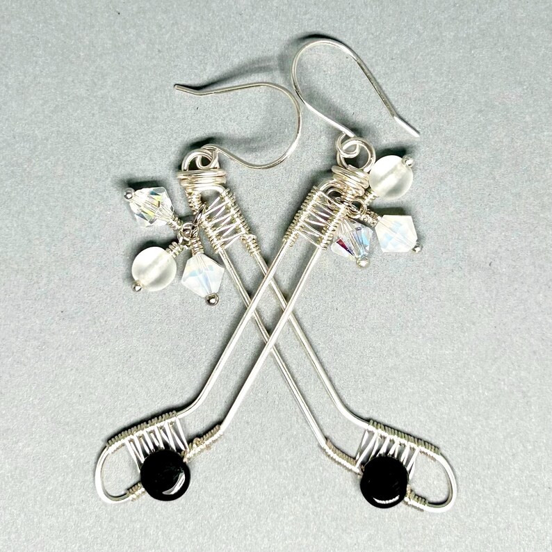 May include: A pair of silver wire earrings shaped like hockey sticks with black and clear beads.