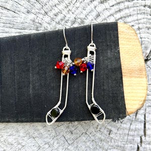 May include: A pair of silver wire earrings shaped like hockey sticks with black and clear beads at the bottom and red, orange, and blue crystal beads at the top.