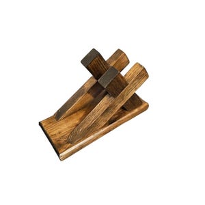 May include: A wooden wine bottle holder with a dark brown finish. The holder features a rectangular base with three angled slots to hold wine bottles. The top of the holder has a darker brown accent.