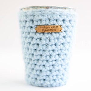 May include: A light blue crocheted cup cozy with a brown leather tag that says "handmade with leytalicious" and a heart symbol.