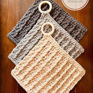 Op de afbeelding: Drie gehaakte ovenwanten in grijs, lichtgrijs en beige, met bevestigde houten ringen. De ovenwanten zijn op elkaar gestapeld, met de beige aan de onderkant. De afbeelding bevat de tekst "CROCHET PATTERN INSTANT PDF DOWNLOAD".