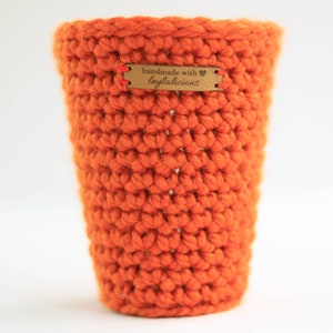 May include: Orange crocheted cup cozy with a brown leather tag that says "handmade with ♥ leylalicious".