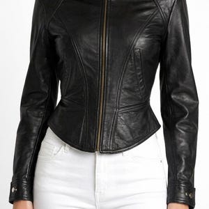 Pode incluir: Casaco de couro preto com gola alta e fecho de correr. O casaco tem uma silhueta ajustada com detalhes de costura e uma cintura peplum. As mangas t&ecirc;m punhos abotoados. A modelo est&aacute; a usar cal&ccedil;as de ganga brancas.