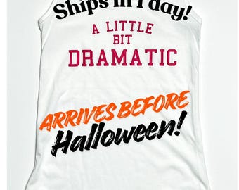 May include: A white racerback tank top featuring the text "Ships in 1 day!", "A LITTLE BIT DRAMATIC" in red, and "ARRIVES BEFORE Halloween!" in orange and black. The straps are embellished with small, clear, reflective rhinestones.