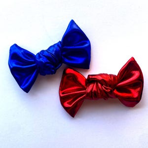 May include: Two metallic hair bows, one blue and one red, tied in a knot. The bows are made of a shiny, satiny material.