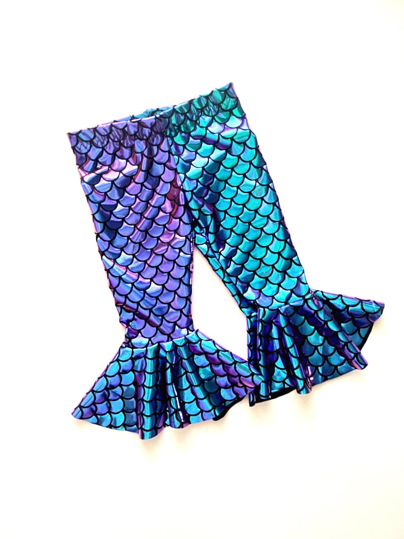Puede incluir: Un par de leggings con tem&aacute;tica de sirena con un patr&oacute;n de escamas en tonos morados, azules y turquesas. Los leggings tienen un bajo acampanado, creando un efecto de cola de sirena. La tela tiene un acabado brillante e iridiscente.