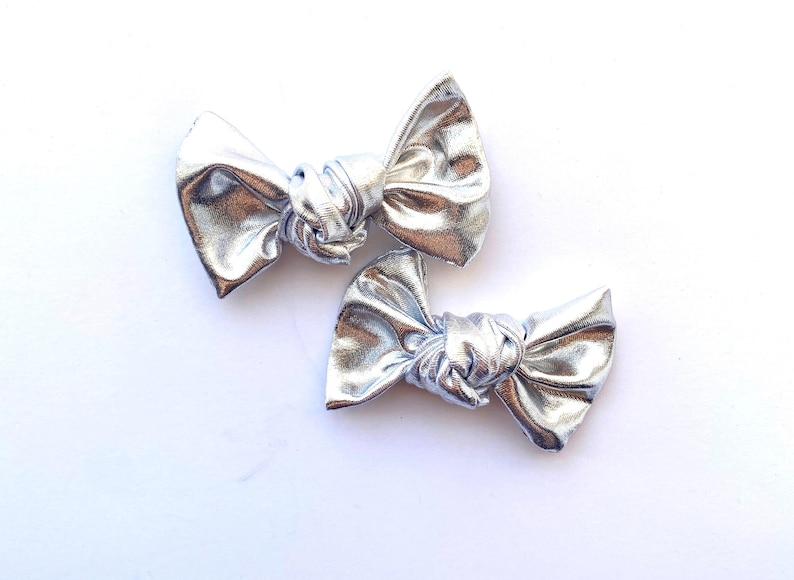May include: Two silver metallic hair bows with a knotted center.