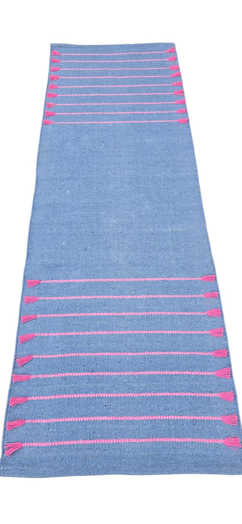 May include: A rectangular blue woven rug with horizontal pink stripes and pink tassels at each end. The rug is made of a textured material and is suitable for use as a runner.