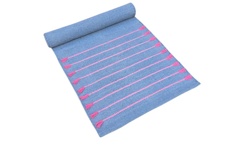 May include: A rolled-up blue rug with pink horizontal stripes and tassels. The rug is made of woven material and is displayed on a white background. The tassels are at the end of each pink stripe.