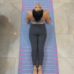 May include: A light blue yoga mat with pink stripes and tassels. The mat is on a tiled floor. The person is wearing a gray sports bra and leggings.