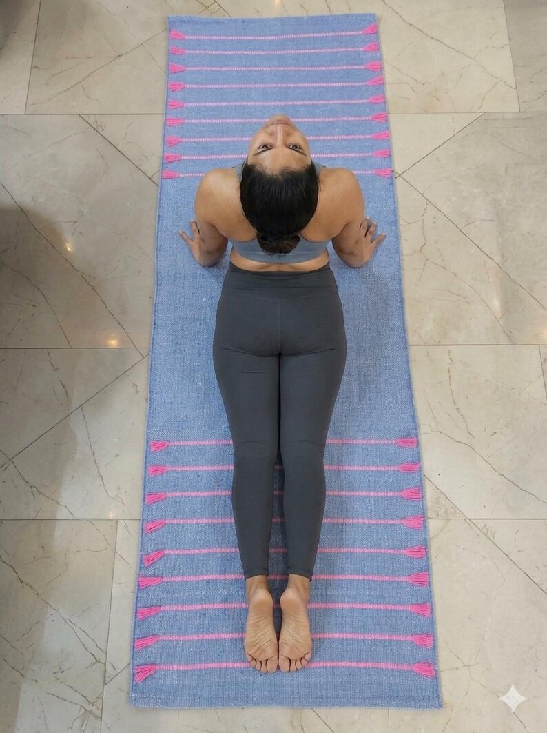 May include: A light blue yoga mat with pink stripes and tassels. The mat is on a tiled floor. The person is wearing a gray sports bra and leggings.