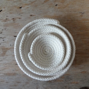 May include: Set of three white rope bowls, nested together in a circular pattern. The bowls are made of natural fiber rope and have a simple, rustic design.