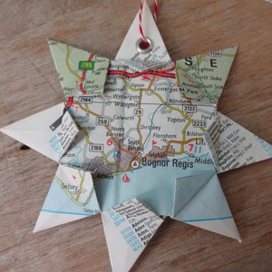 May include: A blue and white paper star ornament made from a map of Bognor Regis, England. The star has a red string attached to it and is decorated with a silver metal ring.