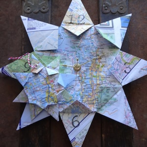 May include: A star-shaped clock made from a map. The clock face is made of paper and has a gold-colored hour and minute hand. The numbers 12, 9, 6, and 3 are visible on the clock face.