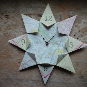 May include: A star-shaped clock made from a map with black hands and numbers 12, 9, 6, and 3.