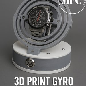 May include: A gray 3D-printed watch winder with a watch inside. The winder has a circular design with a watch holder that rotates. The base is white and gray with a power button. Text on the image reads "3D PRINT GYRO WATCH WINDER STL" and "MFC Design Craft".